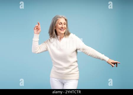 Porträt einer glücklichen, lächelnden Reifen Frau mit geschlossenen Augen, tanzend, Spaß, isoliert auf blauem Hintergrund. Hobby-Konzept Stockfoto