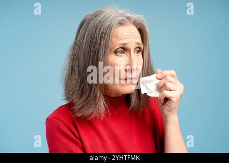 Verärgert, kranke ältere Frau, die kalt ist, in die Kamera schaut, Krankheitfrau, die isoliert auf blauem Hintergrund steht. Behandlung, Gesundheitskonzept Stockfoto