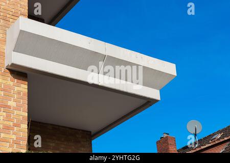 Ein Betonbalkon ragt aus einem Backsteingebäude hervor und präsentiert ein minimalistisches Design. Der hellblaue Himmel unterstreicht die modernen architektonischen Merkmale von Stockfoto