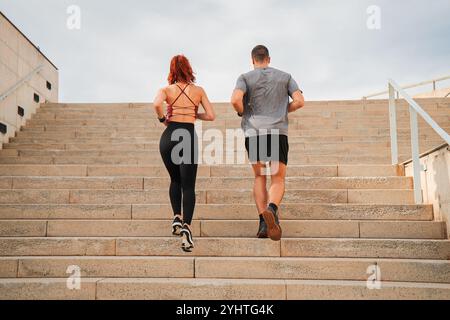Rückansicht eines sportlichen Paares, das während des Cardio-Trainings im Freien Betontreppen mit Sportbekleidung und Sneakers in der städtischen Fitness-Bein-Trainingseinheit hinaufläuft. Hochwertige Fotos Stockfoto