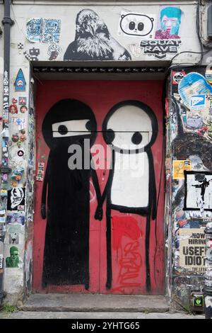 STIK Graffiti Street Artist, Wandkunst, die auf spielerische Weise zwei muslimische Frauen zeigt, eine trägt ihre traditionelle schwarze Abaya und Niqab und die andere ohne Gesichtsbedeckung oder eine weiße Gesichtsbedeckung, die nur die Augen sehen lässt. Gleich neben der Brick Lane, einem Club-Eingang umgeben von Graffiti. Princelet Street, Tower Hamlets, Spitalfields, East End London England Großbritannien 2020er Jahre 2024 HOMER SYKES Stockfoto