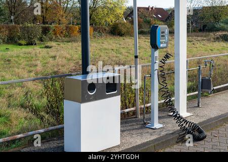 Eine Selbstbedienungs-Waschanlage verfügt über eine Luftpumpe und einen Abfalleimer, die sich in der Nähe eines grasbewachsenen Feldes mit Bäumen und Häusern im Hintergrund auf einer klaren Fläche befindet Stockfoto