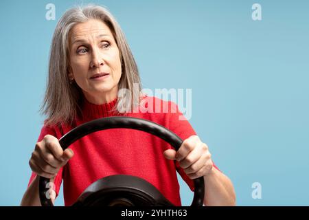 Porträt einer nachdenklichen, Reifen grauhaarigen Frau, Fahrer, der das Lenkrad hält und auf den Kopierraum blickt, isoliert auf blauem Hintergrund posiert. Fahrzeug, t Stockfoto
