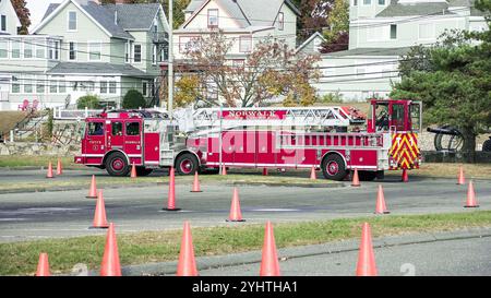 NORWALAK, CT, USA - 7. NOVEMBER 2024: Ein roter Feuerwehrwagen mit verlängerter Leiter steht auf einer asphaltierten Straße in einem Wohngebiet. Orangefarbene Kegel werden platziert Stockfoto