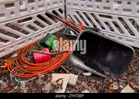 In der Nähe einer Barrikade liegt eine unorganisierte Sammlung von Werkzeugen inmitten von herabfallenden Blättern, mit lebhaften Kabeln und einer Schubkarre, die auf eine neue Außenanlage hindeuten Stockfoto