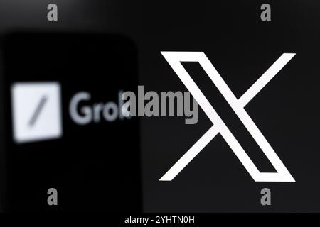 Das Grok-Logo wird auf dem Bildschirm eines Smartphones und im Hintergrund, das Logo des sozialen Netzwerks X (ehemals Twitter) auf dem Computer sc angezeigt Stockfoto