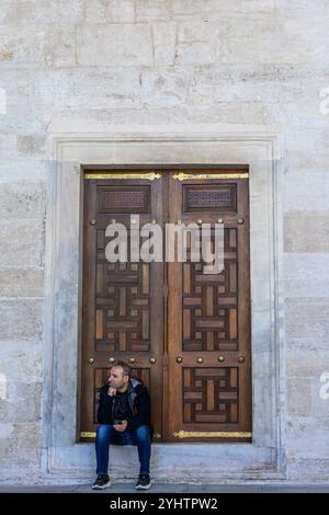 24/10/2024. Die Blaue Moschee, Istanbul, Türkei. Ein Mann sitzt auf der Fensterbank eines verschlossenen Fensters am Rand des Hofes... Die Blaue Moschee, offiziell Sultan Ahmed Moschee (türkisch Sultan Ahmet Camii), ist eine historische Moschee aus der osmanischen Zeit in Istanbul. Sie wurde zwischen 1609 und 1617 unter der Herrschaft von Ahmed I. errichtet und ist heute noch eine funktionierende Moschee. Es zieht auch eine große Anzahl von Touristen an und ist eines der bekanntesten und beliebtesten Denkmäler der osmanischen Architektur. Die Moschee hat einen klassischen osmanischen Grundriss mit einer zentralen Kuppel, die von vier s umgeben ist Stockfoto