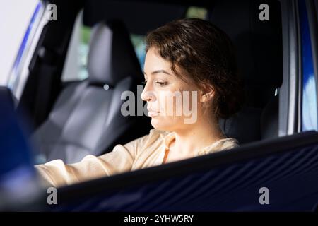 Kunde im Ausstellungsraum des Fahrzeugs überprüft die Fahrzeugfunktionen während der Probefahrt und vergleicht Modelle. Frau, die das Fahrzeug auf dem Parkplatz des Händlerbetriebs fährt, die Haltbarkeit überprüft, auf der Suche nach sachkundigem Kauf ist Stockfoto