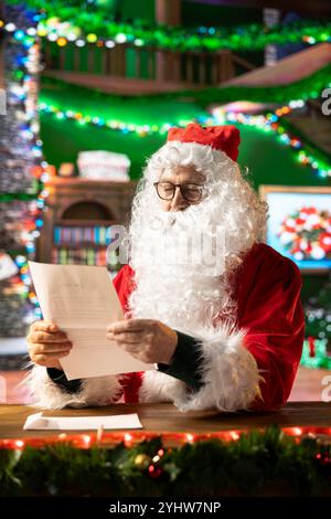 Der Weihnachtsmann liest in seiner gemütlichen Blockhütte Wunschzettel und Briefe, um Weihnachtswunder zu schenken. Mann mit weißem Bart und rotem Anzug erfüllen die Wünsche von Kindern auf der ganzen Welt, Heiliger Nikolaus. Stockfoto