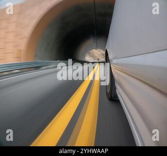 Ein Auto fährt eine Straße mit gelben Linien entlang. Das Auto ist weiß und befindet sich mitten auf der Straße Stockfoto