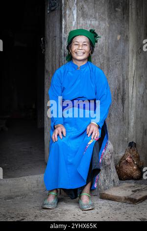 Lächelnde Hmong-Frau, die vor ihrem Haus in der Nähe von Dong Van in der Provinz Ha Giang in Vietnam sitzt Stockfoto