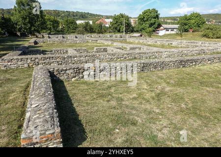 Alte Steinruinen einer römischen archäologischen Stätte in einem ländlichen Grasfeld mit Bäumen und Häusern im Hintergrund: Römisches Castrum „Jidova“ Stockfoto