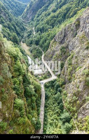 Die sich windende Bergstraße des Staudamms führt durch eine tiefgrüne, bewaldete Schlucht mit steilen Felsklippen auf beiden Seiten, am Vidraru-Staudamm, Transfăgărășan Stockfoto
