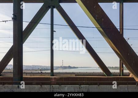 Autos überqueren die Stahlbrücke von Pančevo nach Belgrad (Serbien) über die ruhige Donau, mit einer Stadtlandschaft von Belgrad im Hintergrund Stockfoto