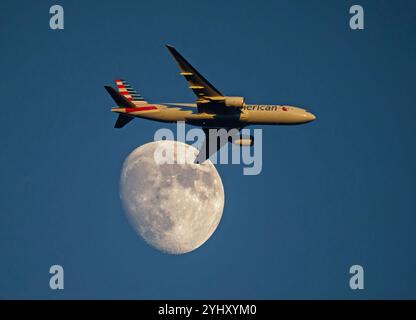 Eine American Airlines Boeing 777 passiert einen Dreiviertelmond bei Sonnenuntergang. Stockfoto