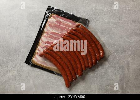 Packungen trockener geräucherter Würstchen und geschnittenem Speck auf grauem Tisch, Draufsicht Stockfoto