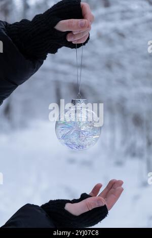 Unerkennbare Frau hängt Weihnachtsdekoration draußen im verschneiten Winterwald. Postkarte Grußkarte Mock Up. Feiertag transparente Kugel Spielzeug Ast Ornamente Neujahrsfeier Stockfoto