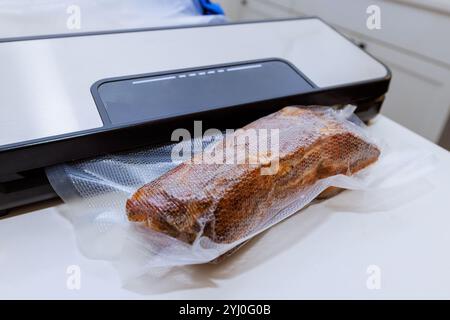 Ein Stück Räucherfleisch wird in einen Vakuumverschlussbeutel gegeben. Dabei wird eine Methode verwendet, um die Lebensmittelqualität zu erhalten und Verderb zu verhindern. Stockfoto