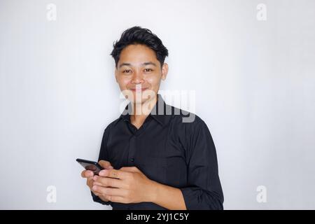 Foto eines hübschen Mannes aus Indonesien, schwarz gekleidet mit einem Handy 13. november 2024 indonesisch Stockfoto