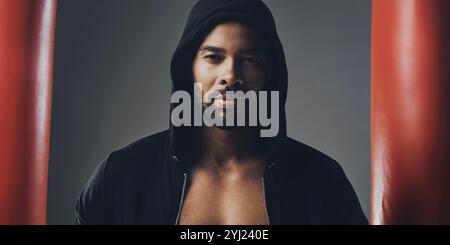 Porträt, Fitness und Mann in Hoodie für Boxen, Sport oder Boxtaschen auf grauem Studiohintergrund. Gesicht, Sport und afrikanischer Boxer, selbstbewusster Athlet Stockfoto