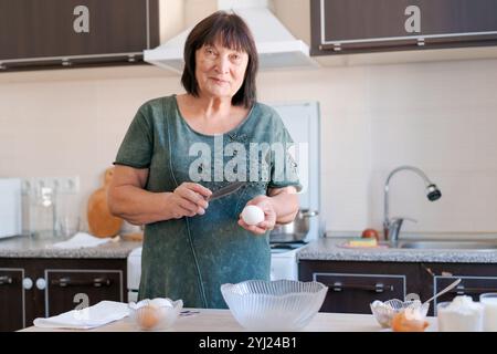 Die Frau schneidet ein Ei in einer Küche. Sie trägt ein grünes Hemd und hält ein Messer Stockfoto