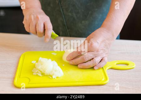 Die Frau schneidet Zwiebeln auf einem gelben Schneidebrett. Sie schneidet die Zwiebeln mit einem Messer in kleine Stücke Stockfoto