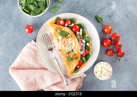 Gefülltes Omelette mit Tomaten, Käse und Spinat auf blauem Hintergrund. Draufsicht. Stockfoto