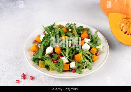 Kürbissalat mit Rucola, Fetakäse und Granatapfelkernen auf grauem Hintergrund. Draufsicht. Thanksgiving-Gerichte. Stockfoto