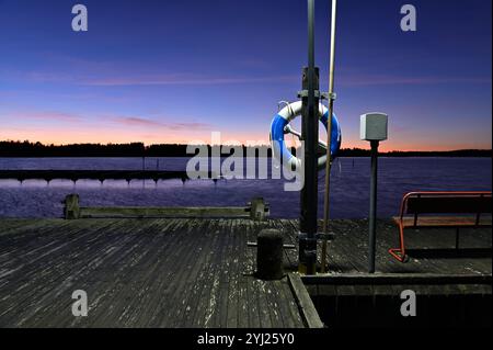 Eine ruhige Hafenlandschaft am See bei Sonnenuntergang oder Dämmerung, mit einem leuchtenden Himmelsverlauf, der von Orange und Rosa am Horizont zu tiefblauem Himmel übergeht Stockfoto