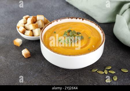 Kürbissuppe mit cremiger, seidiger Textur, Kürbiskernen, frischem Thymian, Croutons auf braunem Hintergrund. Stockfoto