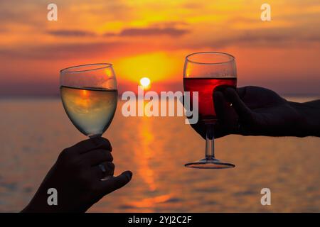 Ein Mann und eine Frau zünden an einem dramatischen Sonnenuntergangshimmel. Weingläser bei Sonnenuntergang am Strand. Selektiver Fokus. Silhouette von zwei Händen Stockfoto