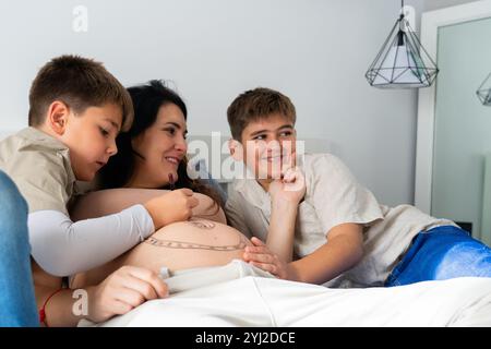 Kaukasische Familie schwangere Mutter mit ihren beiden Kindern, die sich zu Hause den Bauch malen Stockfoto