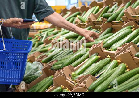 Ein reifer Mann pflückt frische Gurken im Supermarkt aus nächster Nähe. Stockfoto