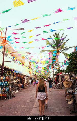 Farbenfrohe Papelpicado-Banner flattern über einer belebten Marktstraße mit Souvenirläden, während eine Frau von der Kamera weggeht. Stockfoto