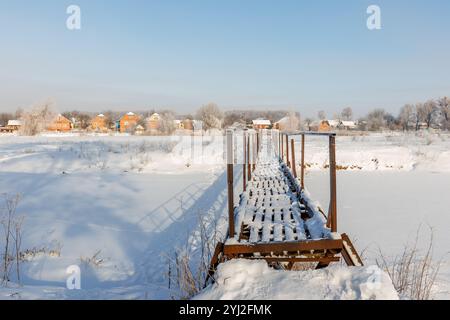 Verschneite Fußgängerbrücke über den Fluss, Winterlandschaft mit Bäumen und Schnee, Frost auf den Bäumen. Stockfoto