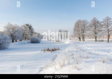 Der gefrorene Fluss ist mit Eis und Schnee bedeckt, die Bäume sind mit Frost bedeckt. Stockfoto