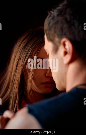 Ein intimer Moment zwischen einer jungen Frau und einem Mann, während sie ihre Augen schließt und ihre Stirn gegen seine lehnt, in sanftem Licht gebadet. Stockfoto