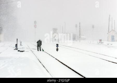 Schneebedeckte Eisenbahn im Winter. Schneebedeckte Bahngleise während eines Schneesturms. Ein Mann reinigt ein Eisenbahngleis mit einem Besen Stockfoto