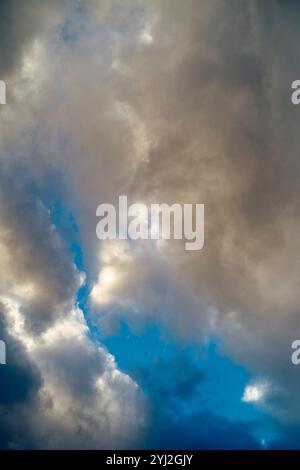 Sonnenlicht bricht durch dynamische blaue und graue Wolken in einem dramatischen Himmel. Stockfoto