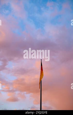 Eine deutsche Flagge flattert auf einem Fahnenmast vor dem Hintergrund eines farbenfrohen Sonnenuntergangshimmels mit Rosa- und Blautönen, Berlin, Deutschland Stockfoto