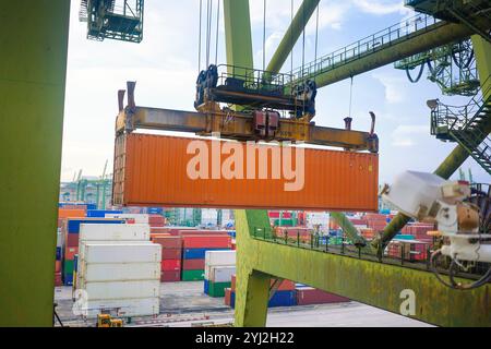 Container, der von einem Kran an einem Frachthafen bewegt wird, mit verschiedenen Containern, die im Hintergrund gestapelt sind, Singapur Stockfoto