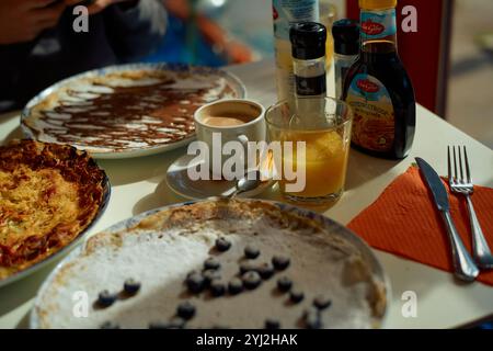 Ein köstliches Frühstück mit frischen Crepes mit Belag, einer Tasse Kaffee und einem Glas Orangensaft auf dem Tisch. Stockfoto
