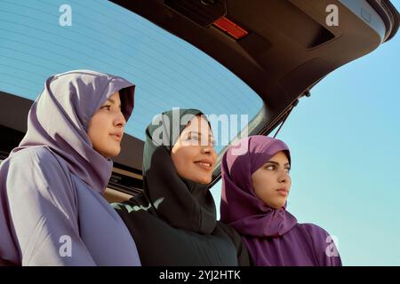 Drei Frauen in farbenfrohen Hijabs, die an einem sonnigen Tag in Marokko in die Ferne von der Rückseite eines Autos blicken Stockfoto
