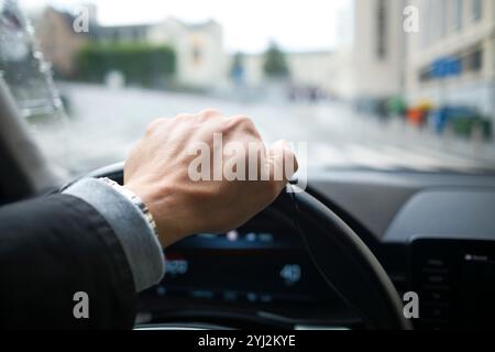 Nahaufnahme der Hand eines Mannes am Lenkrad eines Autos, das durch eine Stadtstraße fährt, Brüssel, Belgien Stockfoto