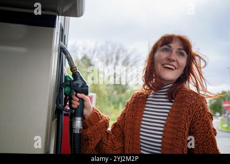 Lächelnde Frau mit rotem Haar betankt ihr Auto an einer Tankstelle in Brüssel, Belgien Stockfoto