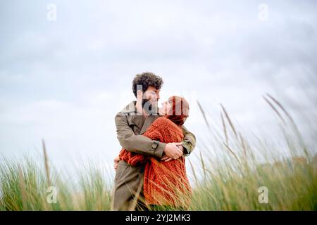 Paare umarmen und küssen auf einem grasbewachsenen Feld unter einem bedeckten Himmel, Belgien Stockfoto