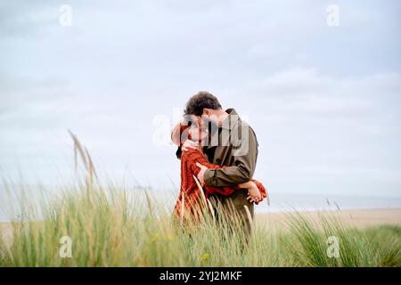 Ein Paar, das sich an einem grasbewachsenen Strand unter einem bewölkten Himmel umgibt, Belgien Stockfoto