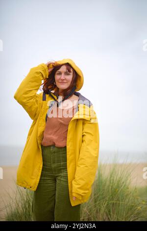 Frau in gelbem Regenmantel, die an einem Strand mit bewölktem Himmel steht, Belgien Stockfoto
