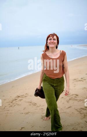 Lächelnde Frau, die an einem bewölkten Tag an einem Sandstrand spaziert, Belgien Stockfoto