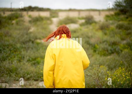 Frau in gelbem Regenmantel, die an einem bewölkten Tag durch die Sanddünen läuft, Belgien Stockfoto